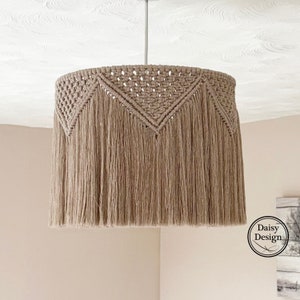 May include: A beige macrame lampshade with a fringe border and a geometric pattern. The lampshade is hanging from a white ceiling.