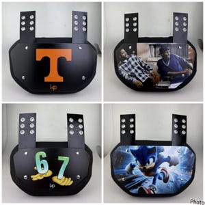 May include: Four black football shoulder pads with different designs. One pad has an orange "T" and the text "kp". Another has a photo of two men. The third has the numbers "67" and the text "kp". The last has a Sonic the Hedgehog graphic.