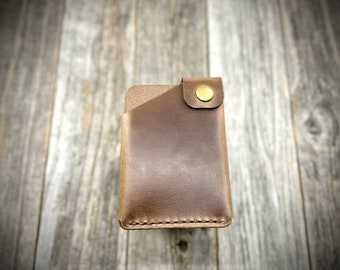 May include: A brown leather wallet with a gold button closure. The wallet is on a wooden background.
