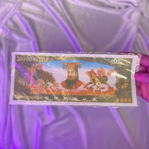 Könnte beinhalten: Ein rechteckiger Geldschein mit goldenen Akzenten, der ein zentrales Porträt eines Mannes mit Bart und dekorativem Kopfschmuck zeigt. Der Schein zeigt Bilder eines Phönix und eines Fabelwesens. Der Text "50000000000" ist sichtbar.