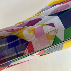 Pu&ograve; includere: Primo piano di una scultura di carta origami colorata con un motivo a quadri blu visibile all'interno. La carta &egrave; piegata in una forma complessa con pi&ugrave; strati.