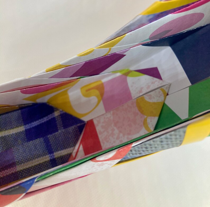 Pu&ograve; includere: Primo piano di una scultura di carta origami colorata con un motivo a quadri blu visibile all'interno. La carta &egrave; piegata in una forma complessa con pi&ugrave; strati.