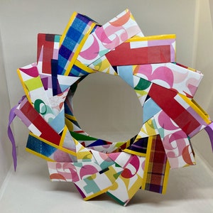 Pu&ograve; includere: Una ghirlanda di carta colorata con un nastro viola. La ghirlanda &egrave; fatta di strisce di carta con diversi motivi e colori, tra cui rosso, giallo, blu, verde e rosa.