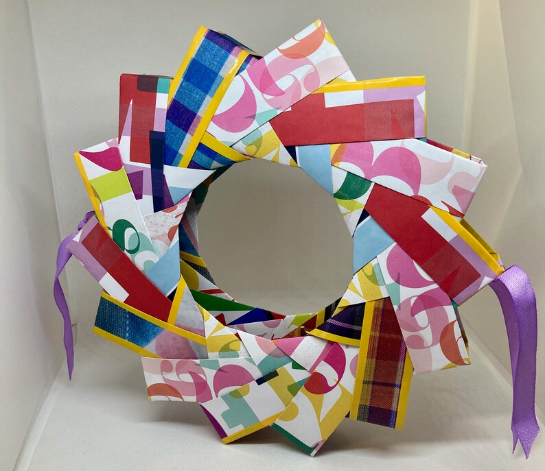 Pu&ograve; includere: Una ghirlanda di carta colorata con un nastro viola. La ghirlanda &egrave; fatta di strisce di carta con diversi motivi e colori, tra cui rosso, giallo, blu, verde e rosa.