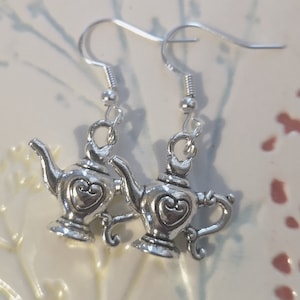 May include: Silver teapot earrings with a heart design. The earrings are on a white background.