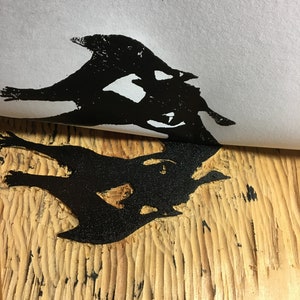 May include: Black ink print of a stylized bird design on a light wood surface.