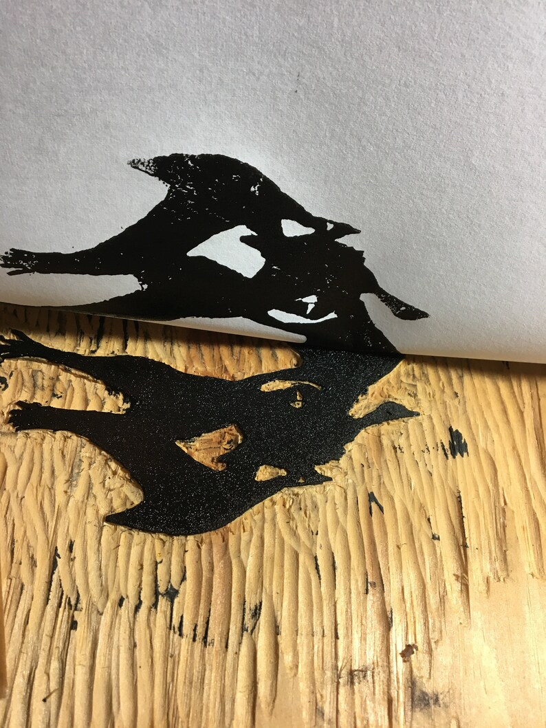May include: Black ink print of a stylized bird design on a light wood surface.