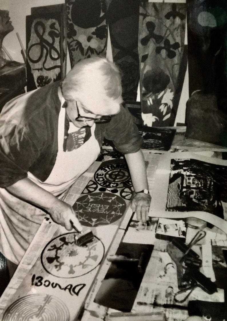 May include: A person in a white apron is working on a black and white print with a brush. The print is circular and has the words "Dance!" written on it. The person is surrounded by other prints and tools.