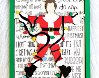 May include: A green framed wood sign with a cutout of a man dressed as Santa Claus tangled in Christmas lights. The sign features text from the movie 'Christmas Vacation' including the quote 'You serious, Clark? Shitter's full!'