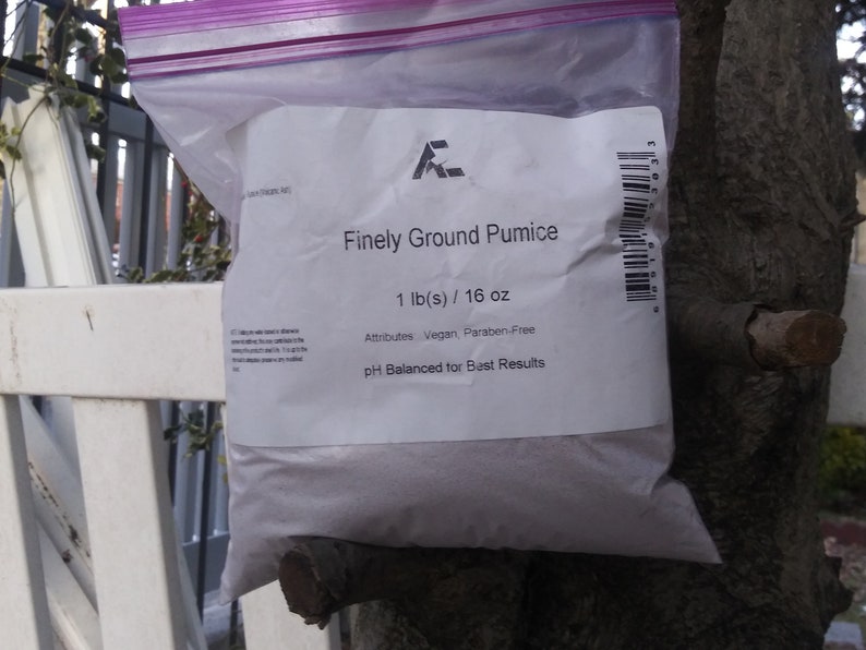 May include: A white resealable plastic bag containing finely ground pumice. The bag is labeled with the text "Finely Ground Pumice", "1 lb(s) / 16 oz", "Attributes Vegan, Paraben-Free", and "pH Balanced for Best Results".