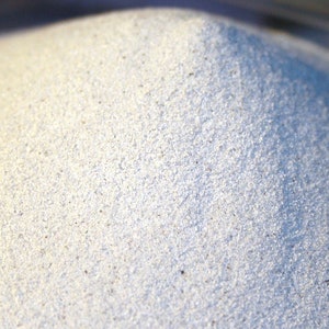 May include: A close-up of a pile of white sand. The sand is fine-grained and has a slightly grainy texture.
