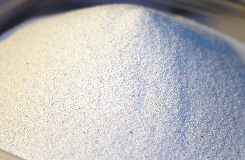 May include: A close-up of a pile of white sand. The sand is fine-grained and has a slightly grainy texture.