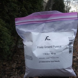 May include: A white resealable bag containing finely ground pumice. The bag is labeled with the text "Finely Ground Pumice", "1 lb(s) / 16 oz", "Attributes: Vegan, Paraben-Free", and "pH Balanced for Best Results".