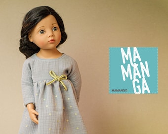 May include: A doll wearing a light blue dress with gold polka dots and a gold ribbon tied at the waist. The dress has long sleeves and a gathered skirt. The doll has brown hair and brown eyes. The background is a light brown wall with a blue square with the text "MAMANGA" in white.