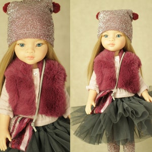Puede incluir: Una muñeca con un gorro rosa brillante con pompones rojos, un chaleco de piel sintética burdeos, un bolso de rayas rosa y blanco y una falda de tul gris.