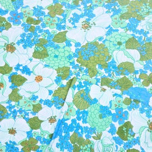 May include: A fabric featuring a dense floral pattern in shades of bright blue, light turquoise, and olive green on a white background. The design includes large white blossoms with orange centres, clusters of small blue flowers, and green leaves.