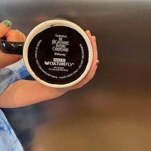 May include: Black ceramic mug featuring the text "Tim Burton's The Nightmare Before Christmas" and the Disney logo. The mug is built by Culturefly and is marked as hand wash only and not microwave safe.