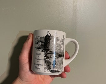 May include: White ceramic mug with a black and white illustration of Castillo de San Marcos in St. Augustine, Florida.