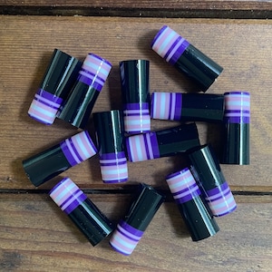 May include: A collection of 11 black and purple striped cylindrical objects. The objects are made of glass and have a glossy finish.