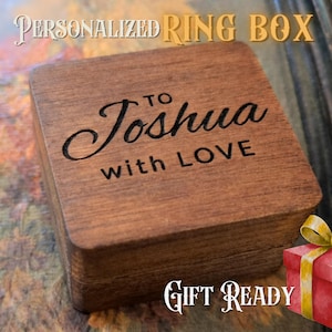 Może przedstawiać: Kwadratowe drewniane pudełko na pierścionek z napisem "PERSONALIZED RING BOX" na g&oacute;rze. Pudełko jest grawerowane napisem "TO Joshua with LOVE". Małe czerwone pudełko na prezent ze złotą wstążką znajduje się w rogu. Słowa "GIFT READY" znajdują się na dole.