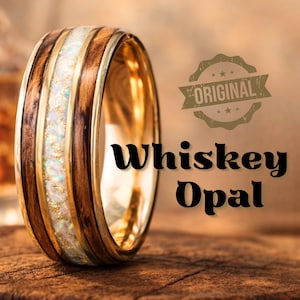 May include: A close-up of a ring with a wooden and opal design. The ring features alternating bands of dark brown wood and white opal with gold accents. The text "Whiskey Opal" is displayed below the ring.