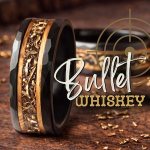 May include: A black hammered metal ring featuring a central inlay of light brown wood and metallic gold-colored fragments. The text "Bullet WHISKEY" is overlaid on the image, accompanied by a circular target graphic with crosshairs.