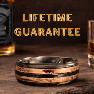 May include: A ring featuring a polished dark metal band with two inlaid textured wood segments. The text LIFETIME GUARANTEE is displayed in orange letters above the ring, which is positioned between two glass containers.