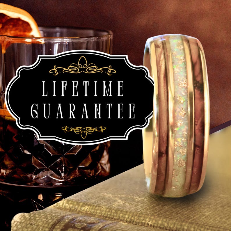 May include: A ring featuring a central band of iridescent white opal inlay flanked by two dark brown wood grain sections and gold-toned metal edges. A black rectangular label with gold decorative borders displays the text LIFETIME GUARANTEE.