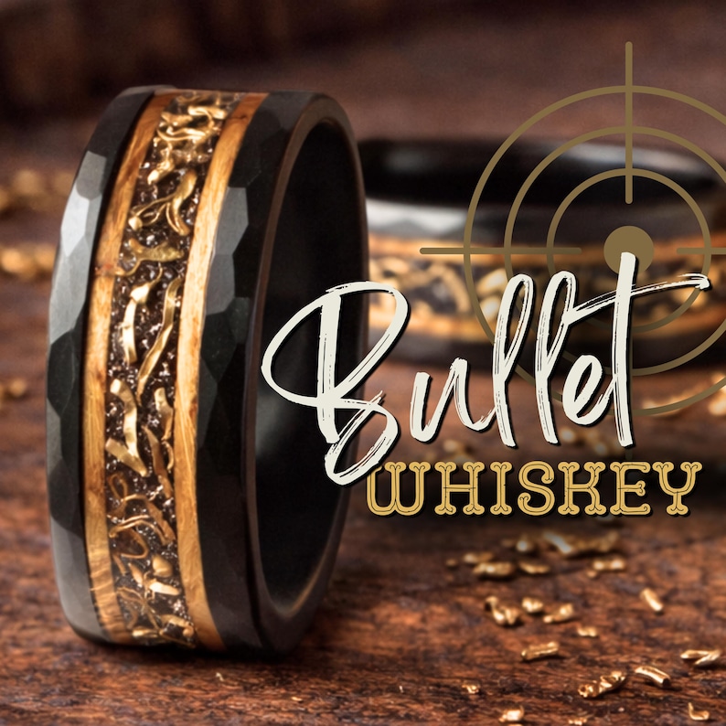 May include: A black hammered ring featuring a central inlay of wood and metallic fragments. The text "Bullet WHISKEY" is overlaid on the image alongside a gold crosshair graphic. The ring has a dark, textured exterior and a smooth inner band.