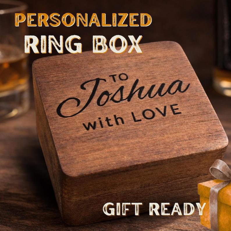 May include: A square, dark brown wooden ring box featuring the engraved text "TO Joshua with LOVE" on the lid. The box has a smooth, polished finish and a hinged design, presenting a clean, simple aesthetic for storing small jewelry items.