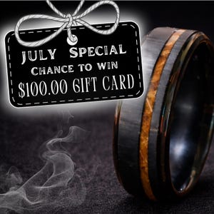 Puede incluir: Un anillo negro con una incrustaci&oacute;n central de material marr&oacute;n texturizado. Una etiqueta rectangular negra con texto blanco que dice JULY SPECIAL CHANCE TO WIN $100.00 GIFT CARD, con un dibujo lineal blanco de un lazo.