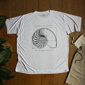 May include: White t-shirt with a black and white graphic of a nautilus shell with the text "Fibonacci discovered it" and "The universe created it".