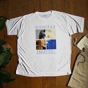 May include: White t-shirt featuring a graphic design with the text "50 YEARS OF BLUE" and "JONI MITCHELL". The design includes four image squares with a portrait of a woman. The shirt is made of a soft, lightweight material.