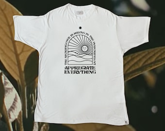 May include: White t-shirt with a black graphic design. The graphic features a sun with a face, waves, and the text "The significance is hiding in the insignificant. Appreciate everything."