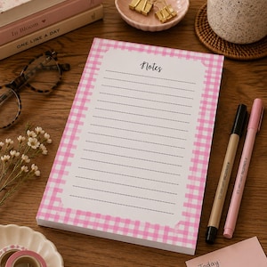 May include: A rectangular notepad featuring a pink and white gingham border and the word Notes printed at the top. The centre contains horizontal dashed lines for writing. The notepad is surrounded by stationery items including pens, washi tape, and a checklist.