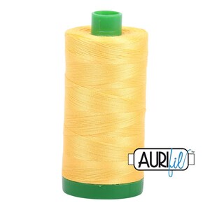 May include: A spool of yellow thread with a green top and bottom. The thread is tightly wound and has a smooth texture. The brand name "AURIfil" is printed on the side.