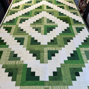 May include: A green and white quilt with a geometric pattern. The quilt is made up of squares and rectangles of different shades of green. The quilt is made in a log cabin style.