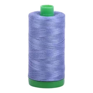 May include: A spool of light blue sewing thread with a green base and top. The thread is tightly wound, showing the texture of the fibers. Ideal for sewing projects, this thread is a versatile crafting supply.
