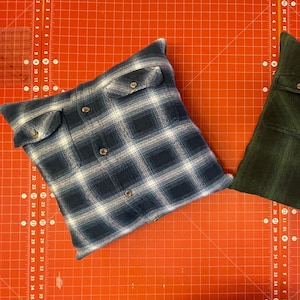 May include: Two decorative pillows made from repurposed flannel shirts. One pillow is blue and white plaid, the other is green and black plaid.