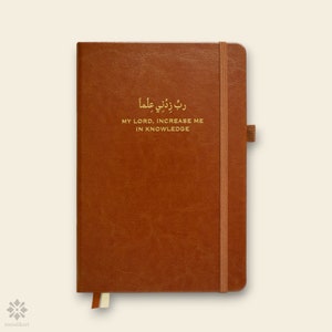 May include: A brown leather-bound journal with a gold elastic closure and a gold inscription that reads "ربي زدني علما" which translates to "My Lord, increase me in knowledge".