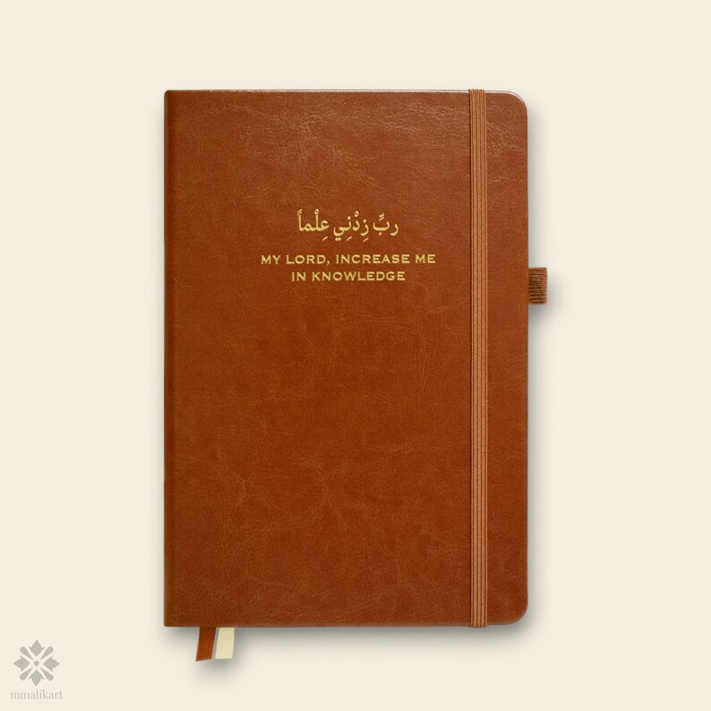 May include: A brown leather-bound journal with a gold elastic closure and a gold inscription that reads "ربي زدني علما" which translates to "My Lord, increase me in knowledge".