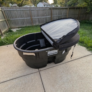 May include: A black plastic 150-gallon Rubbermaid tote with a black and gray cover. The tote is sitting on a concrete patio.