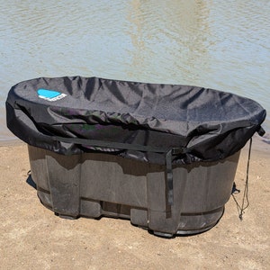 May include: A black plastic tub with a black cover. The tub is sitting on a sandy beach.