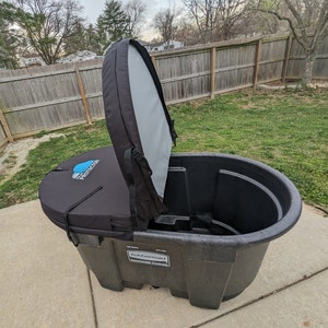 May include: A black and gray plastic tub with a removable, gray fabric lid. The tub has a blue and white label that says "The Protector". The tub is sitting on a concrete surface.