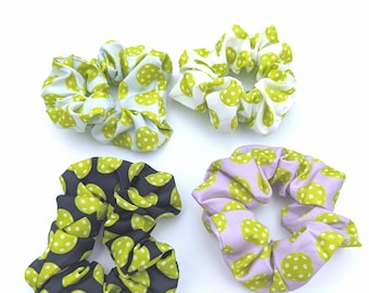 May include: Four fabric scrunchies in various colors and patterns. One is light blue with lime green polka dots, another is white with lime green polka dots, a third is black with lime green polka dots, and the last is lavender with lime green polka dots.