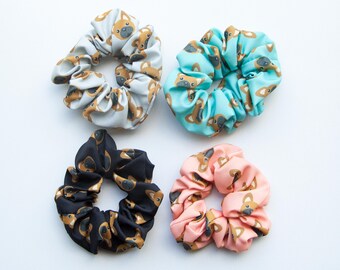 May include: Four fabric scrunchies with a cartoon dog print. The scrunchies are in blue, pink, black, and light blue.