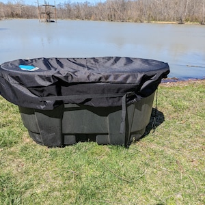 May include: A black plastic hot tub with a black cover. The hot tub is sitting on green grass near a body of water.