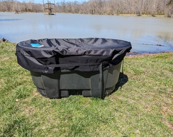 May include: A black plastic hot tub with a black cover. The hot tub is sitting on green grass near a body of water.