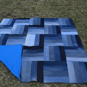 May include: A blue and black patchwork picnic blanket made from recycled denim. The blanket has a blue fleece backing.