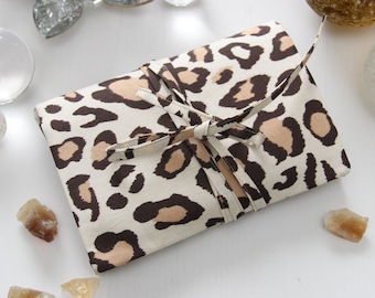 May include: A brown and white leopard print fabric pouch tied with a brown ribbon. The pouch is surrounded by small clear glass orbs and brown crystals.
